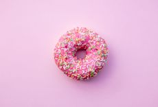 Donut mit pinker Glasur und Streuseln auf pinkem Hintergrund