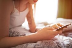 Frau liegt mit ihrem Smartphone in der Hand im Bett