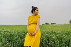 Schwangere Frau steht in einem Feld und hält ihren Babybauch