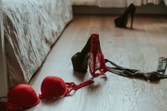 High Heels und rote Dessous auf dem Boden neben einem Bett
