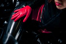 Frau in schwarzem Latexanzug mit roten Handschuhen