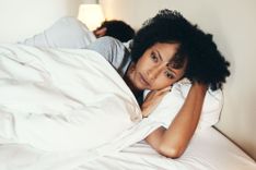 Frau liegt nachdenklich mit dem Rücken zum Partner im Bett