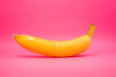 Eine Banane mit einem übergestülpten Kondom vor einem pinken Hintergrund