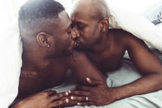 Männliches Pärchen küsst sich unter der Bettdecke