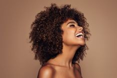 Lachende, freizügige Frau mit Afro vor braunem Hintergrund