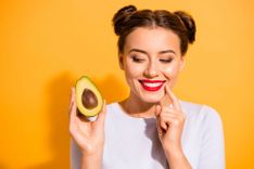 Frau, die eine halbe Avocado in der Hand hält und lächelt