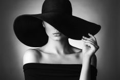 Frau in einem schwarzen Kleid, sie trägt einen großen schwarzen Hut