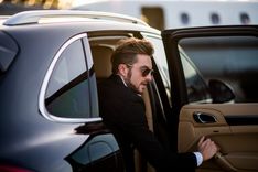 Mann in Anzug und Sonnenbrille steigt in ein Auto mit getönten scheiben