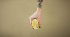 Frau hält eine Zitrone in der Hand, aus der Saft topft