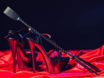 Schwarze High Heels und Reitgerte auf rotem Satinstoff