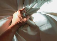 Mann greift die Bettdecke und ballt die Hand zur Faust