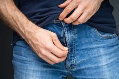 Mann öffnet den Reißverschluss seiner Jeans