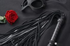 Lederpeitsche, Ledermaske und eine rote Rose