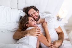Verliebt in Affäre - Abbildung eines glücklich lächelnden Paares, Arm in Arm im Bett.