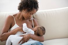 Eine Frau die auf einem Sofa sitzt und ihr Baby im Arm stillt