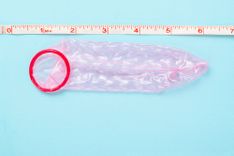 Rosa Kondom neben einem Maßband auf blauem Hintergrund