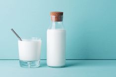 Ein Glas und eine Flasche Milch vor einem hellblauen Hintergrund