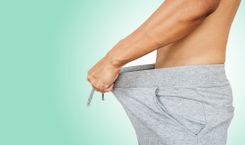 Mann, der am Bund seiner Jogginghose zieht vor grünem Hintergrund