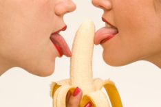 Zwei Frauen mit roten Lippen lecken an einer Banane