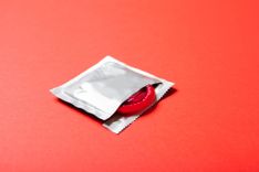 Geöffnete Kondompackung mit Kondom auf rotem Hintergrund