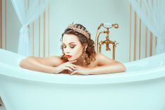 Frau mit Krone sitzt nackt in der Badewanne