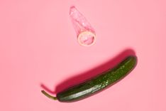 Gurke mit ausgepacktem Kondom auf pinkem Hintergrund