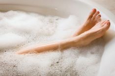 Badewanne mit Schaum aus der zwei Frauenfüße mit lackierten Fußnägeln herausragen