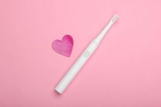 Elektrische Zahnbürste und ein Herz aus Papier auf rosa Hintergrund