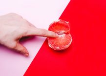 Finger, der in eine rote Grapefruit gesteckt wird auf einem rosa-rot geteilten Hintergrund