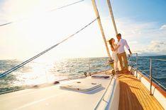 Ein Paar das Arm in Arm auf einem Segelboot steht und in den Sonnenuntergang segelt