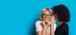 Frau flüstert einer anderen Frau etwas ins Ohr