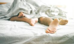 Auf dem Bild sind vier Füße zu sehen, die unter einer zerknüllten Bettdecke hervorschauen.