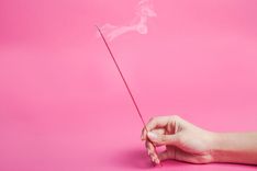 Frauenhand, die ein Räucherstäbchen hält vor pinkem Hintergrund