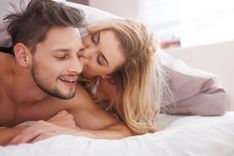Frau küsst die Wange eines Mannes während sie unter einer Decke im Bett liegen