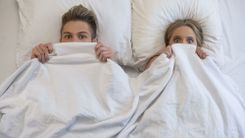 Mann und Frau im Bett haben die Decke bis zu den Augen hochgezogen