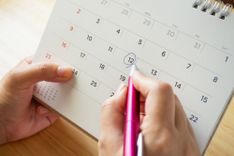 Hände, die einen Kalender halten und mit einem Stift ein Datum einkreisen