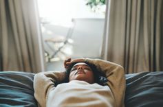 Frau in Pullover, die mit geschlossenen Augen auf einem Bett liegt