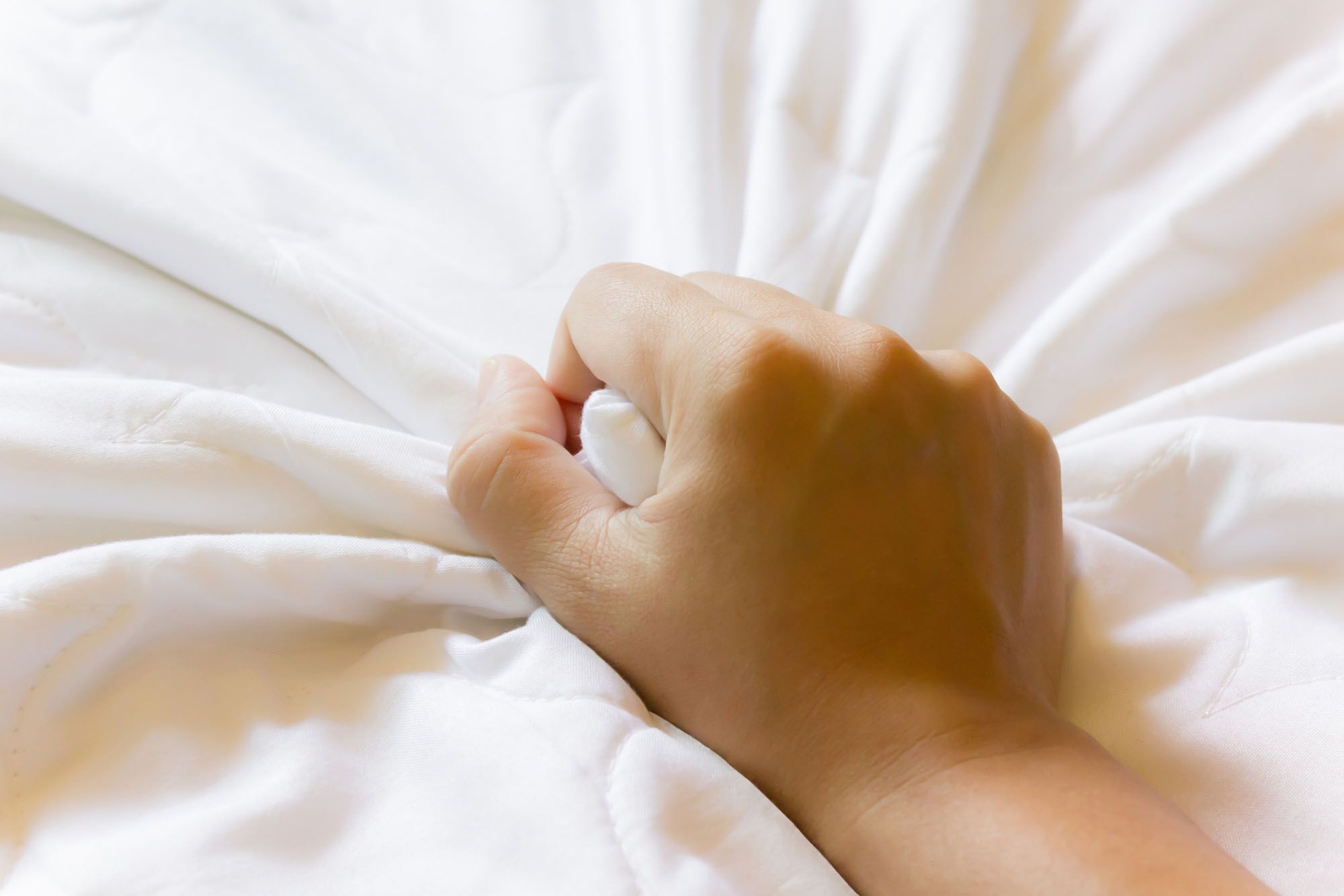 Hand krallt sich in eine Bettdecke