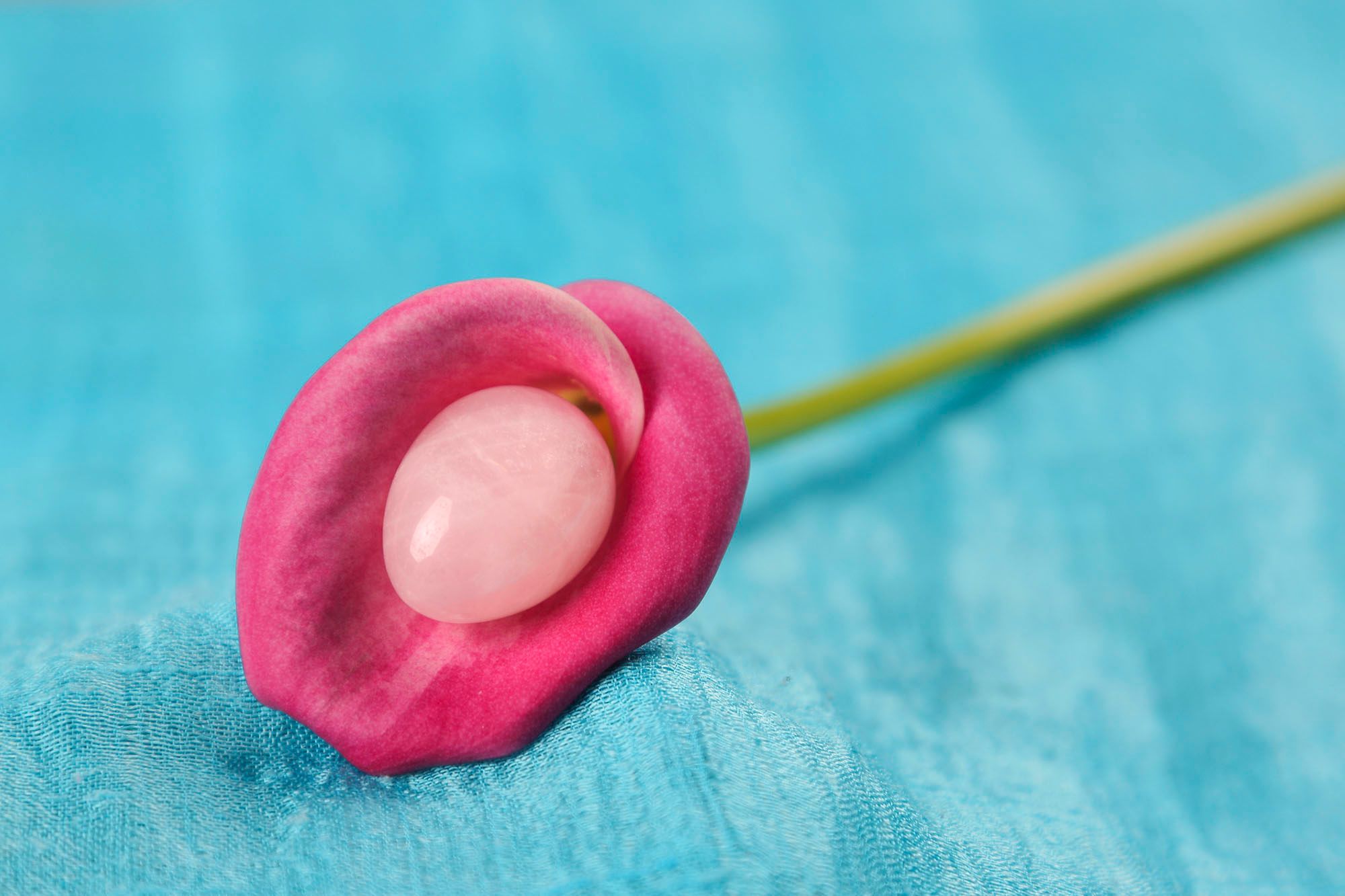 Blüte, in der ein rosa Stein liegt, der Hintergrund ist blau