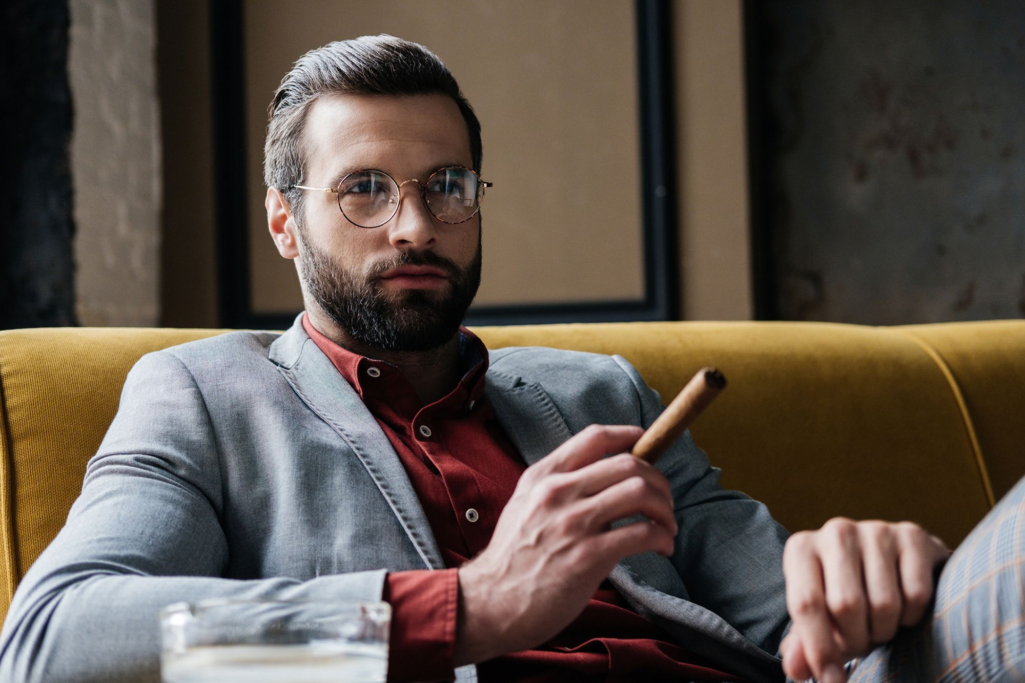 Mann mit Brille, Anzug und Zigarre auf einem Sofa