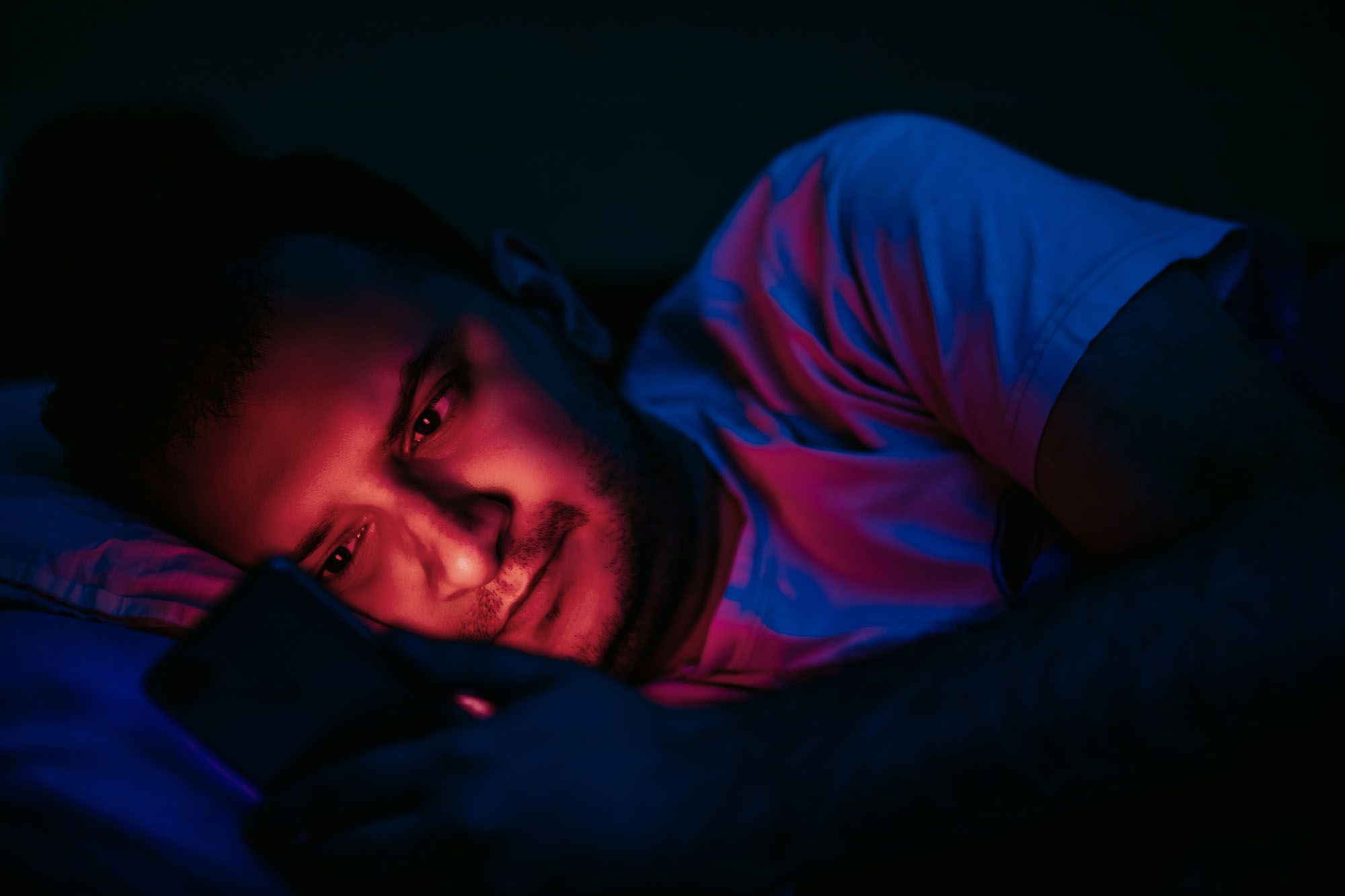 Mann liegt seitlich im Dunkeln im Bett und schaut auf sein Handy
